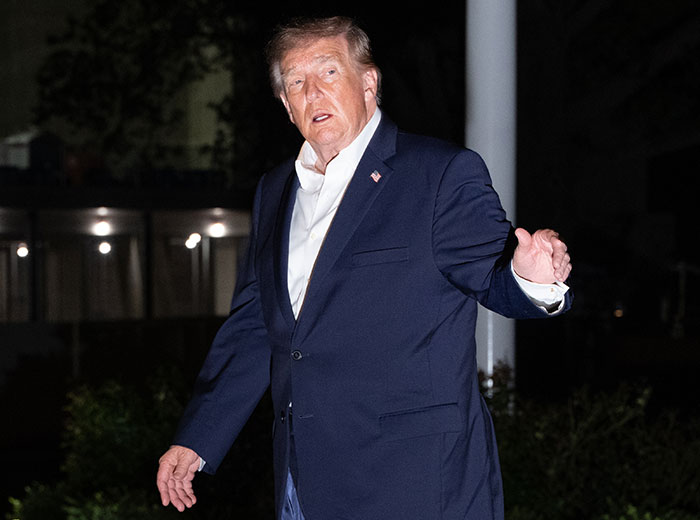 Donald Trump in a dark suit speaking at night on the White House grounds.